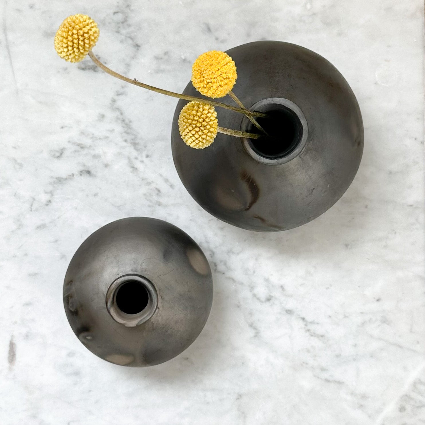 A pair of small and large Oaxaca clay bud vases with dry stems.