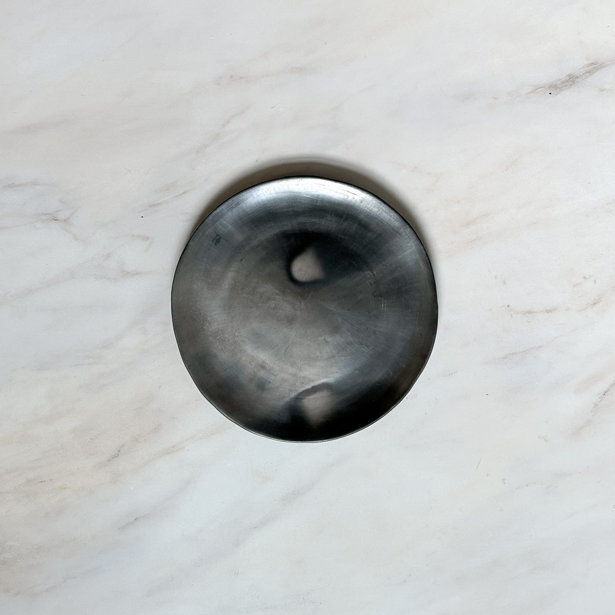 A Oaxaca silvery black clay dinner plate on a marble counter.