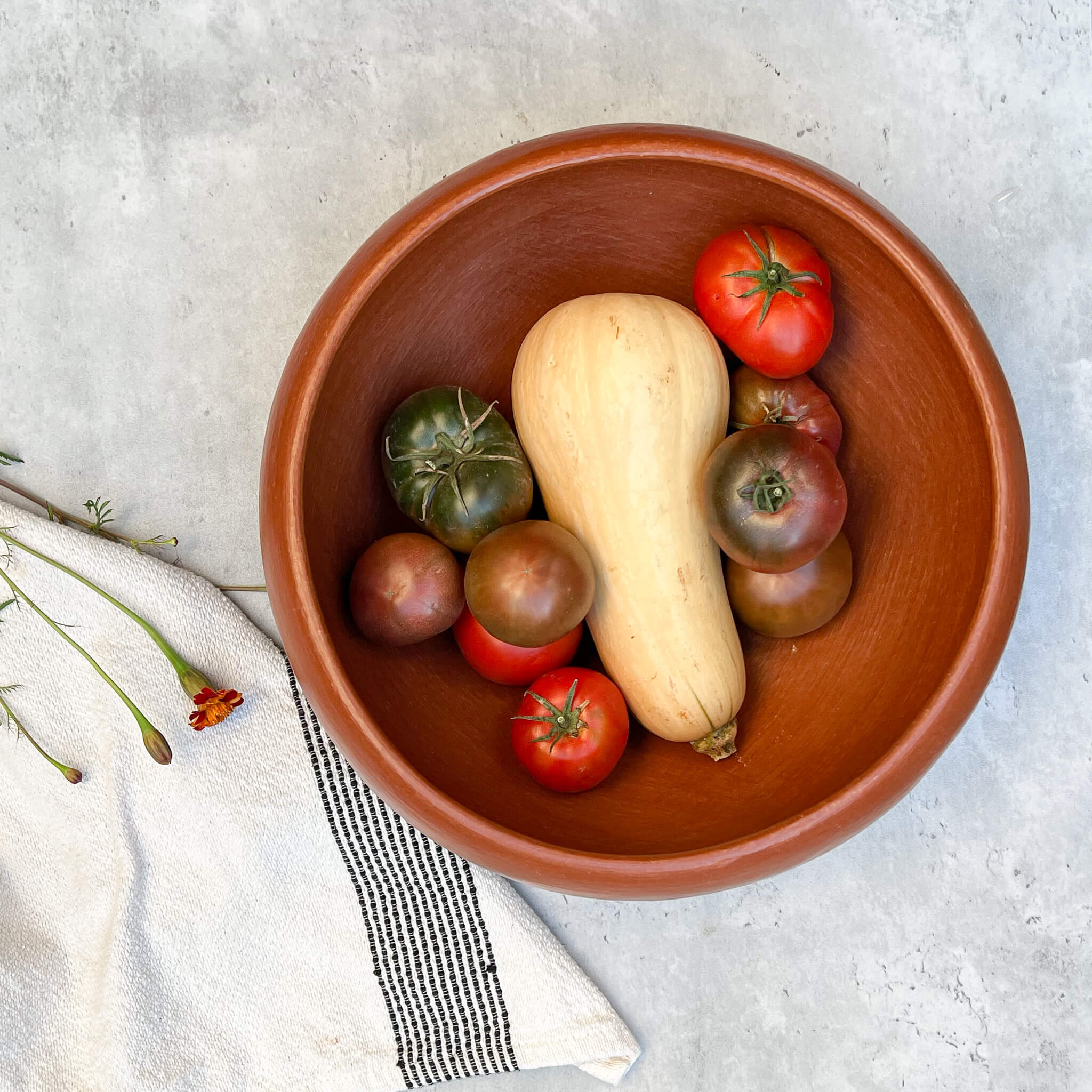 A 12 inch Oaxaca large red clay bowl with a butternut squash and tomatoes