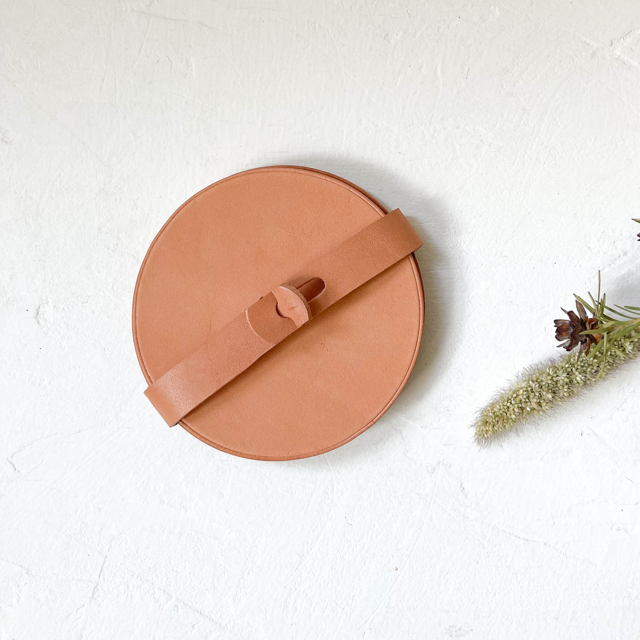 A set of Baja leather coasters in natural nude color shown with a storage strap.