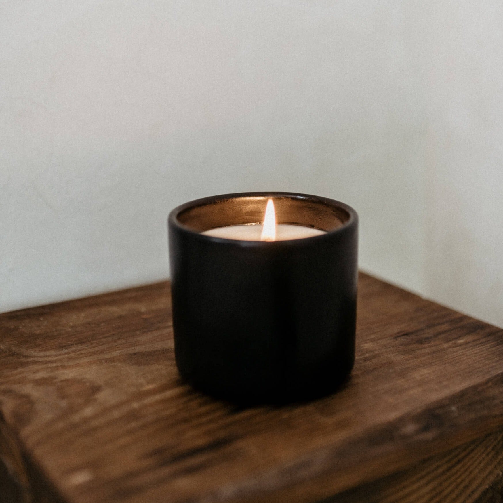 Black ceramic candle on a wood table lit.