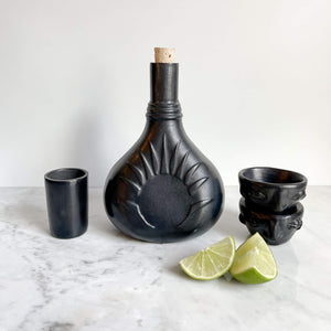 A Oaxaca black clay tequila decanter alongside mezcal copitas and lime slices.