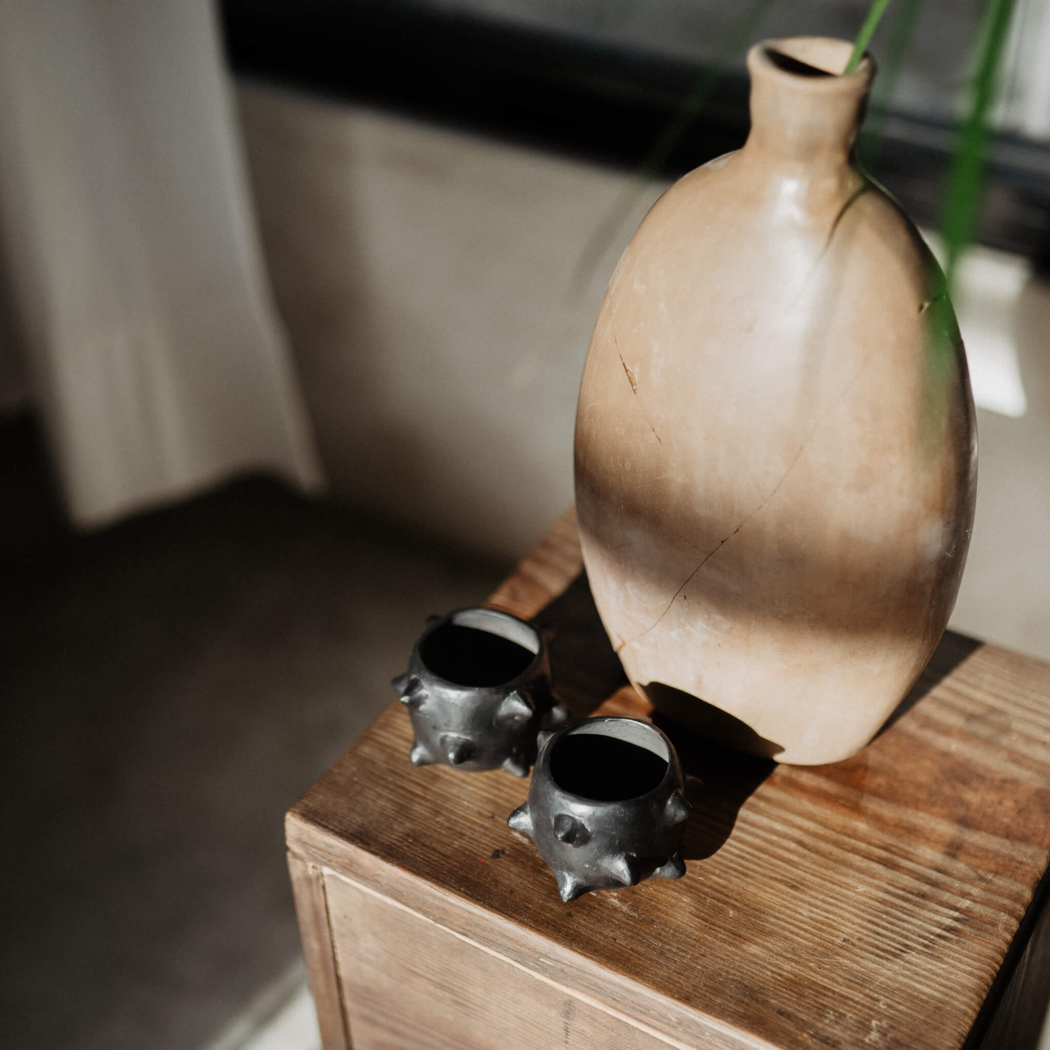 Black clay mezcal copitas next to a vase.