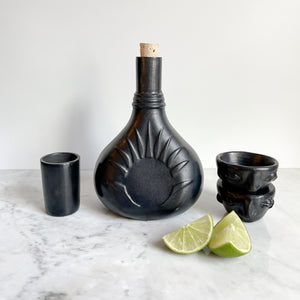 A black clay tequila vessel next to a stack of sliced limes.