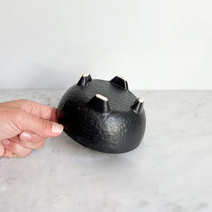 A black mini molcajete bowl touched by a hand.