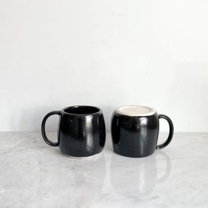 Black stoneware ceramic mugs on a marble counter.