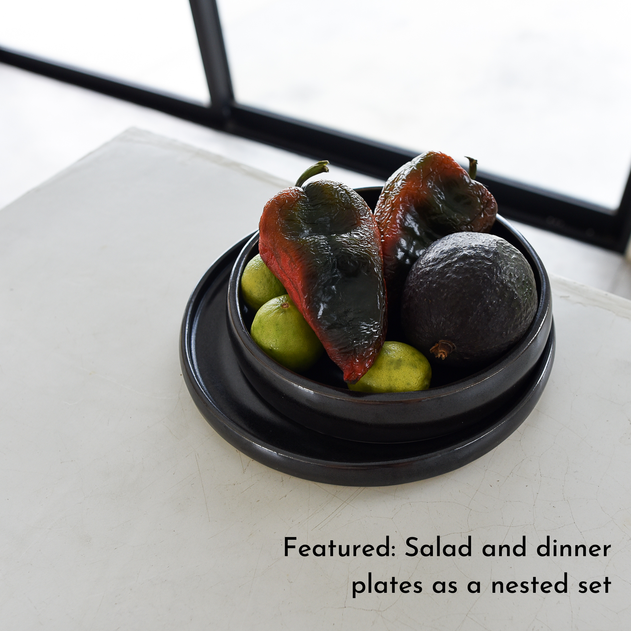 A nested set of black stoneware plates with peppers and fruit.