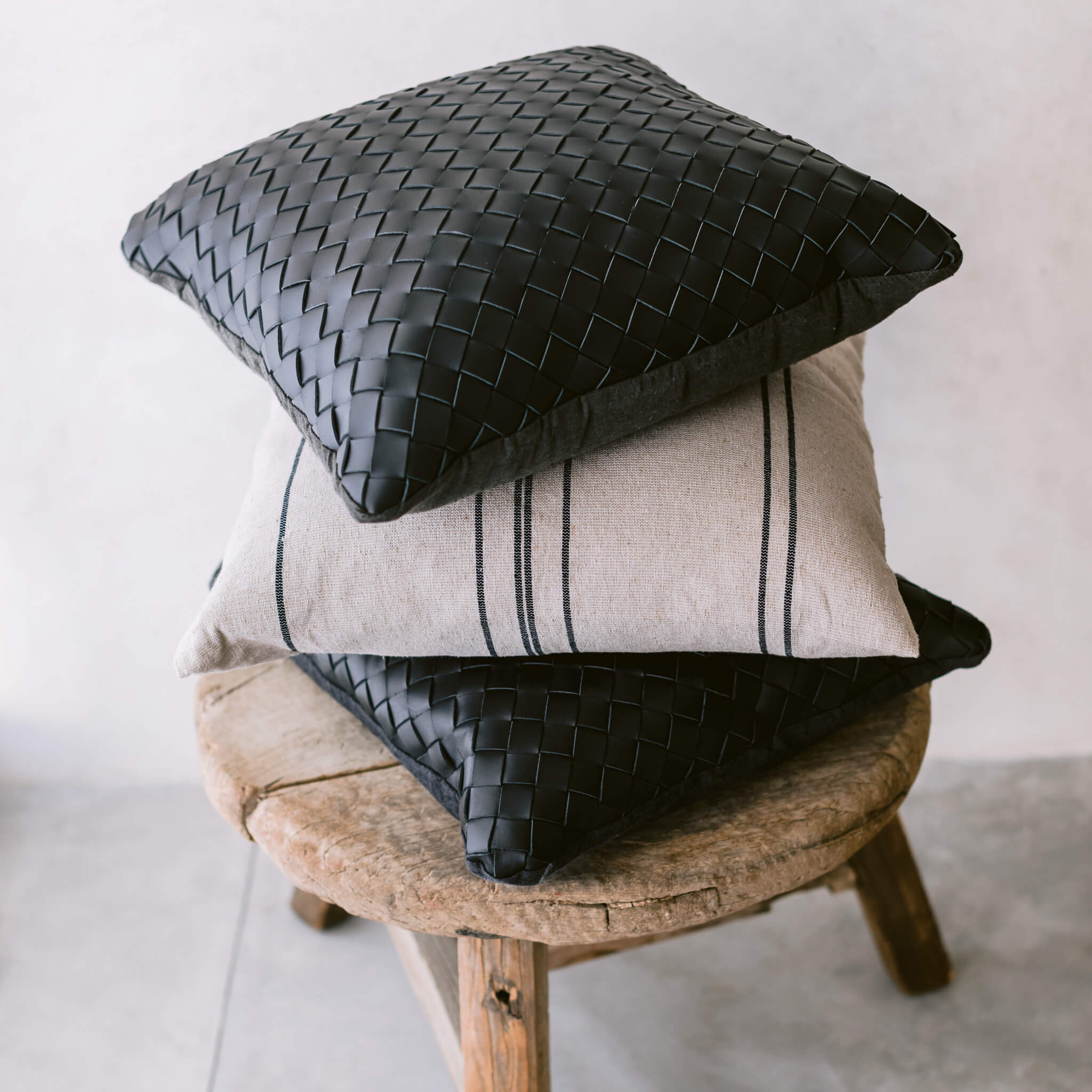 A black braided leather throw pillow stacked on a wood stool.