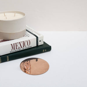 A copper incense holder next to a stack of books and a candle.