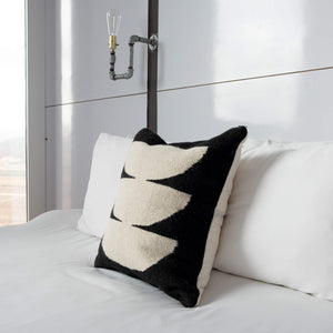A dark moon wool throw pillow handwoven in Oaxaca on a white bed.