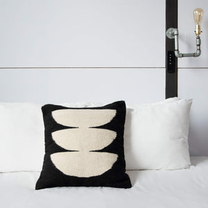 A dark moon wool throw pillow on a white bed.