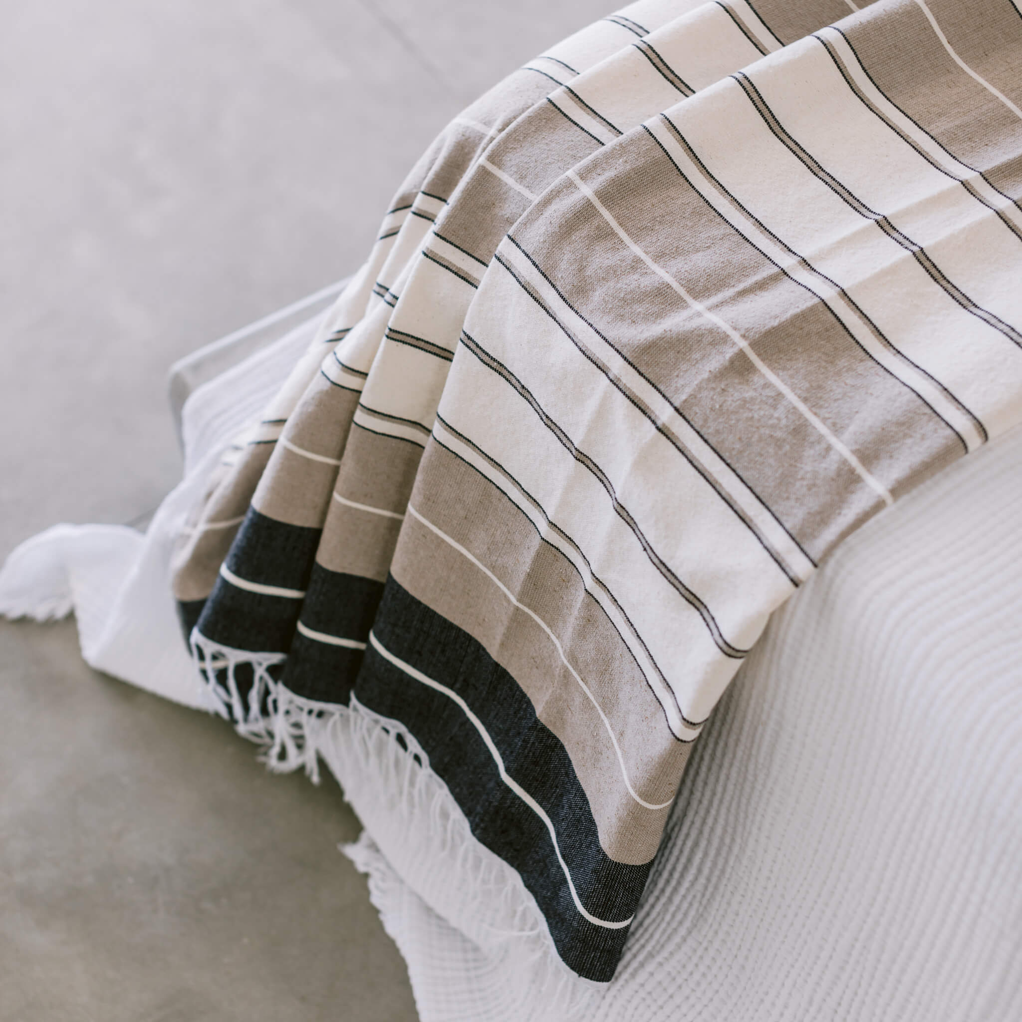 The details on a desert stripes cotton coverlet on the edge of a bed.