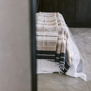 A folded desert stripes cotton coverlet on the end of a bed.