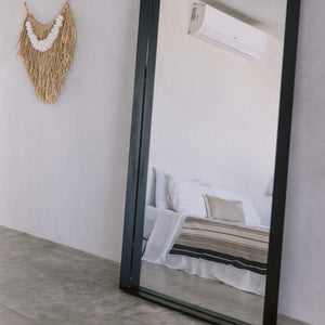 A desert stripes cotton coverlet shown reflected in a mirror next to a fringe palm wall hanging.