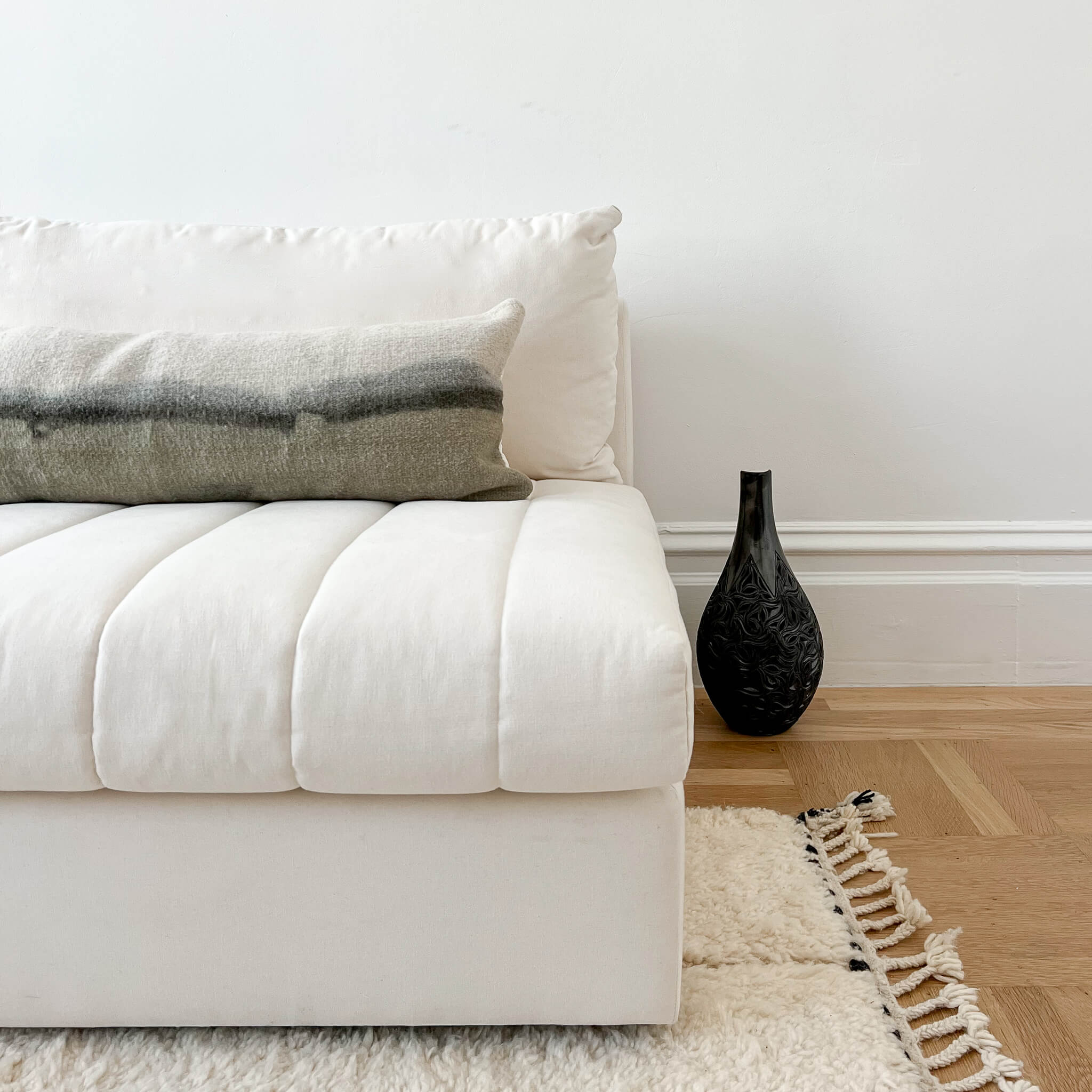 A gradient lumbar pillow on a white couch with a black vase on the floor.