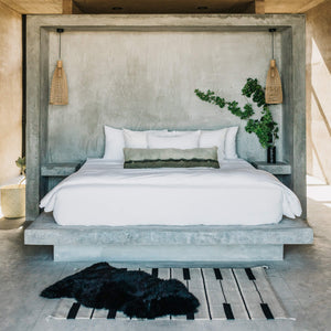 A bedroom in a beach house featuring a large bed, oversized lumbar pillow, and layered wool and sheepskin rugs.