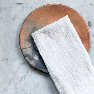 A white Oaxaca cotton napkin against an orange clay plate.