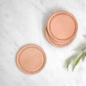 Javier leather coasters in natural on a marble counter.