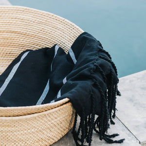 A poolside set of woven palm storage baskets with a black cotton towel.