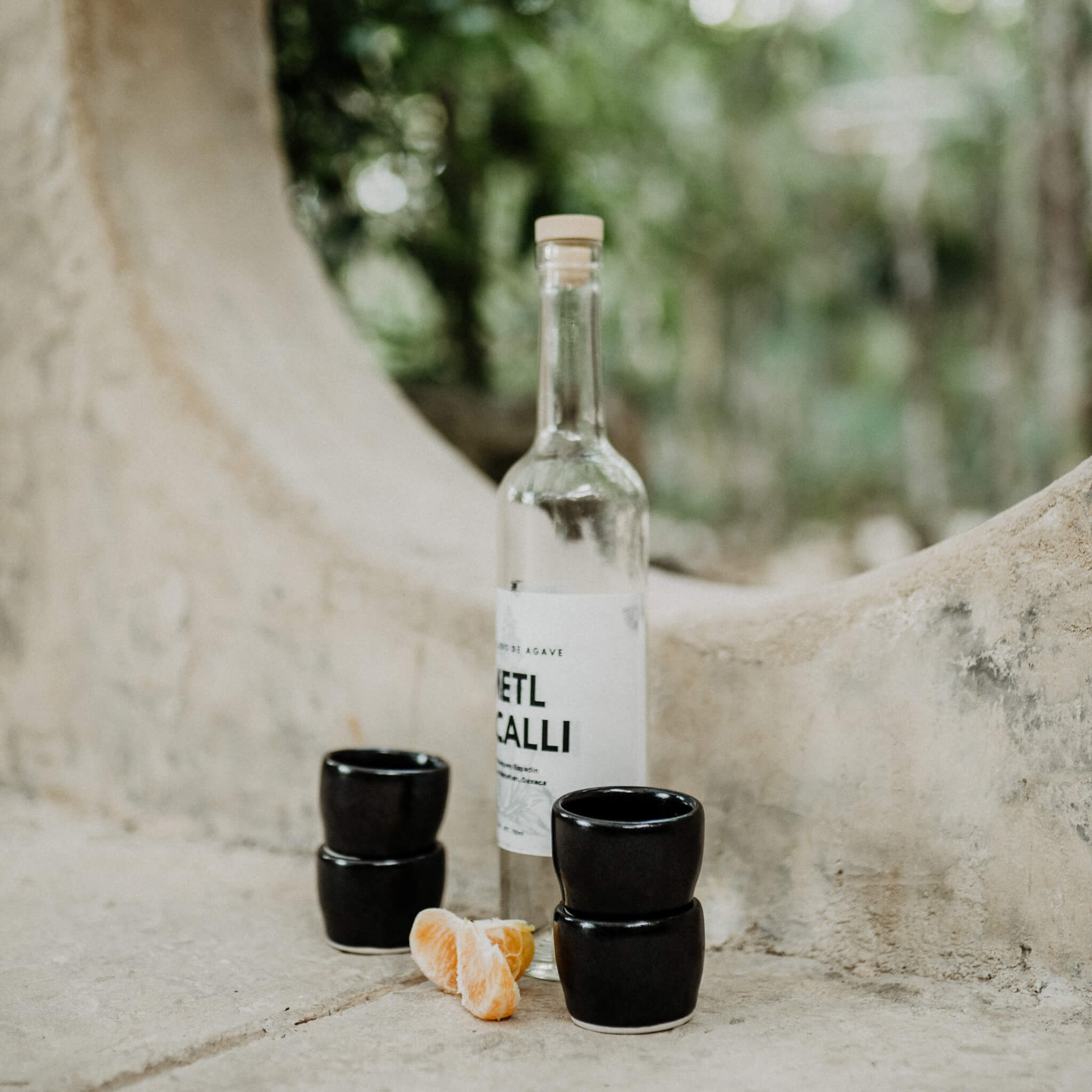A set of black clay mezcal drinking cups with mezcal and orange slices.