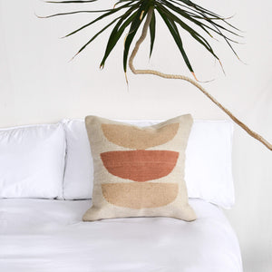 La Rosa wool pillow on a white bed next to a yucca tree.