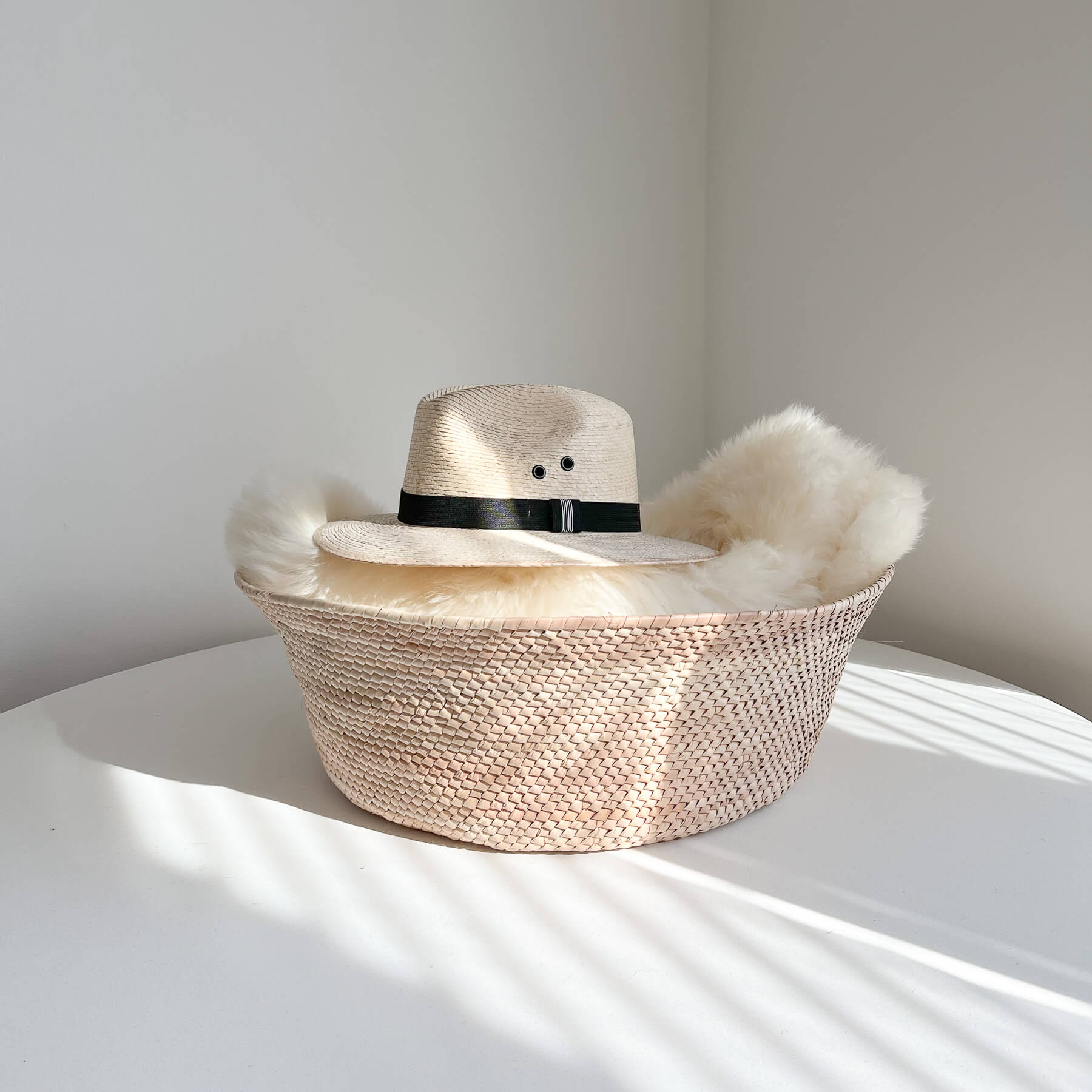 A large palm floor basket made in Mexico storing a sheepskin throw and Mexican palm hat.
