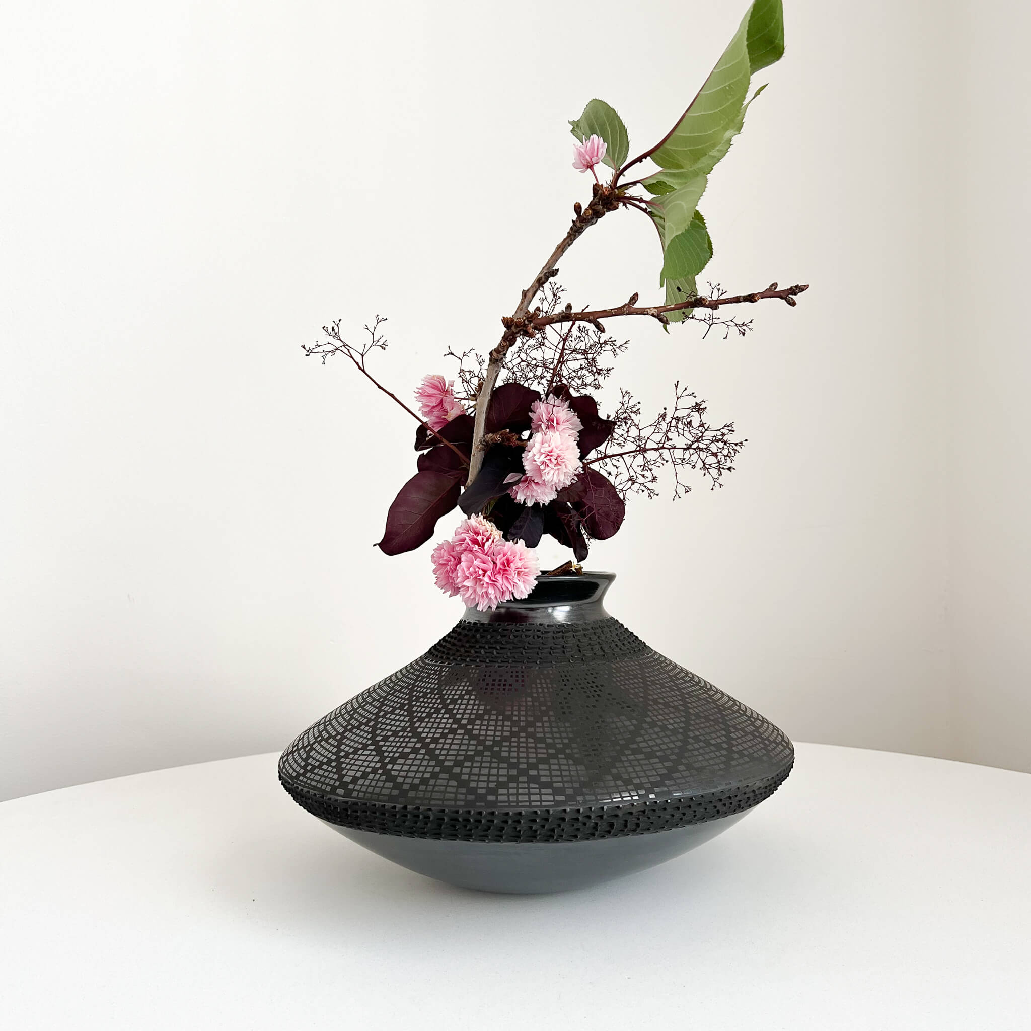 A Mata Ortiz spheroid shaped vase with dry stems and florals.