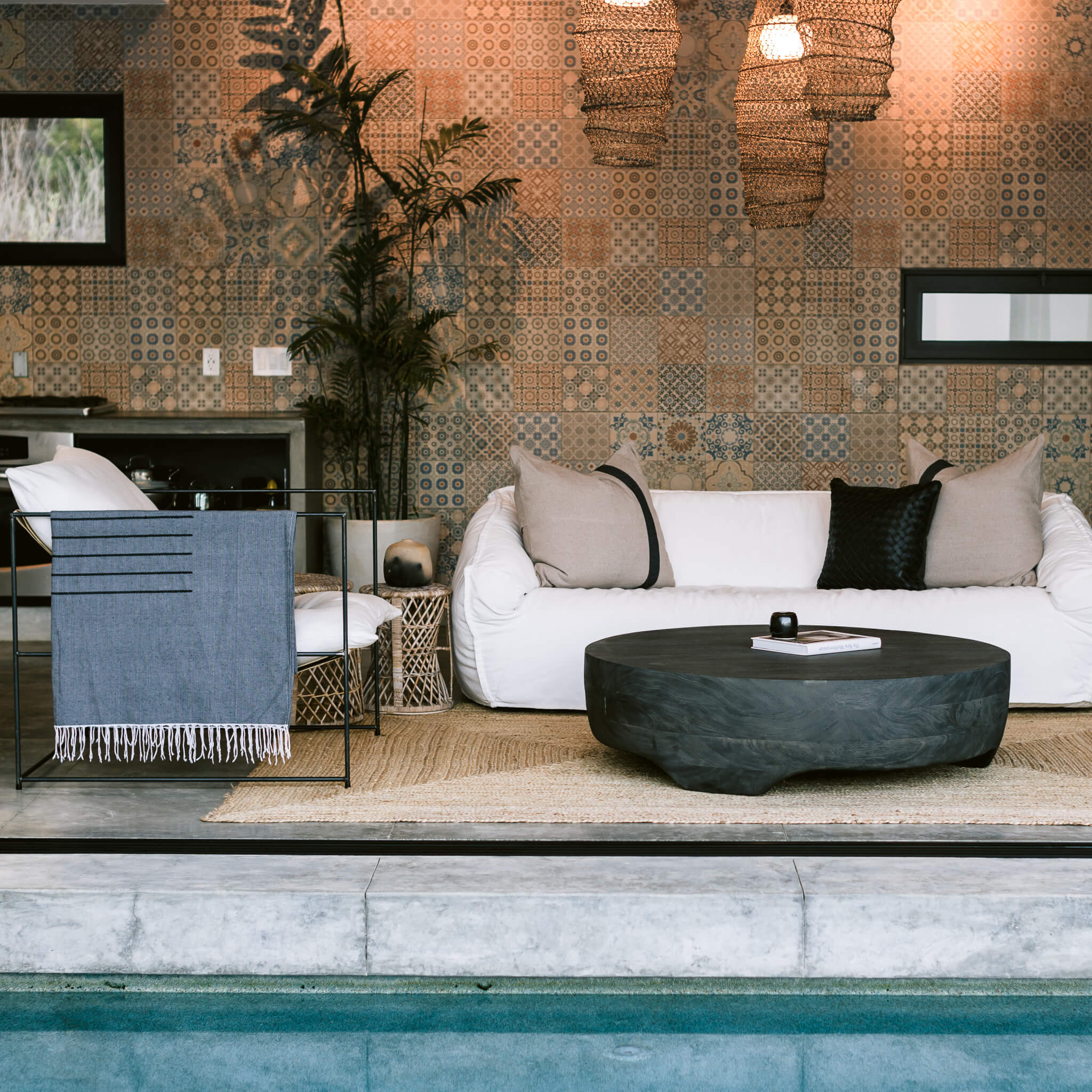 An open concept, Mediterranean-style home featuring doors leading to the pool, a white overstuffed couch and a tiled wall. A black braided throw pillow is arranged on the white couch.