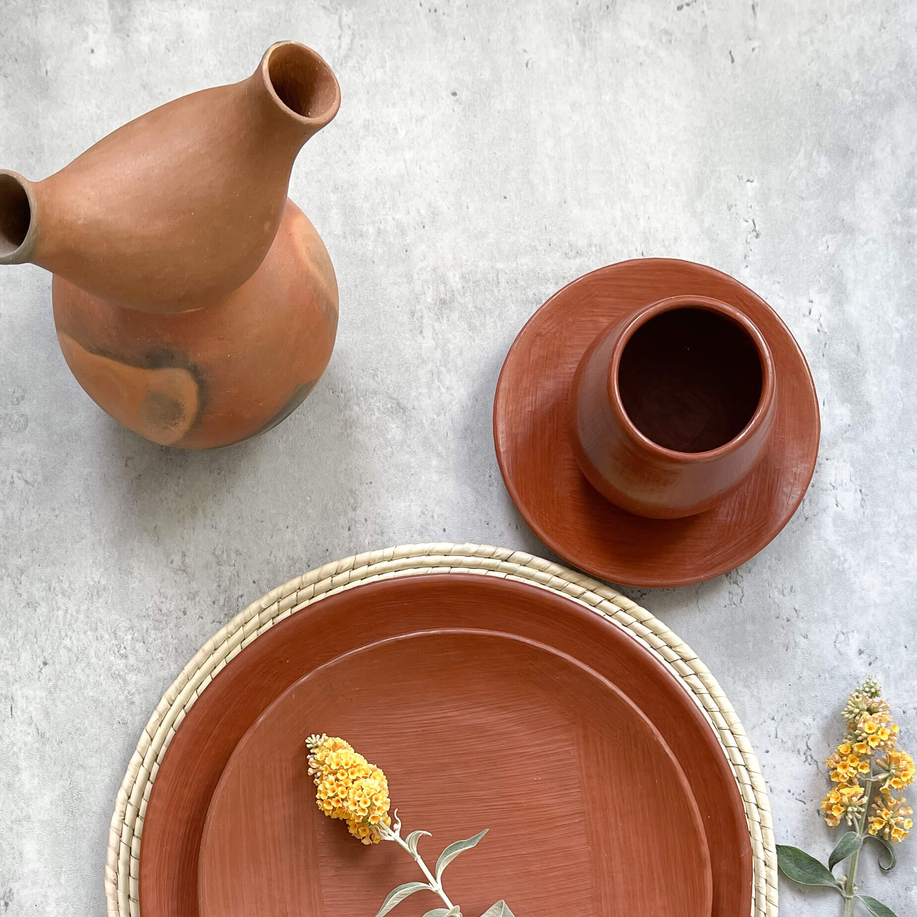 An assortment of Mexican red clay pottery including plates, a mug and a decorative vase.