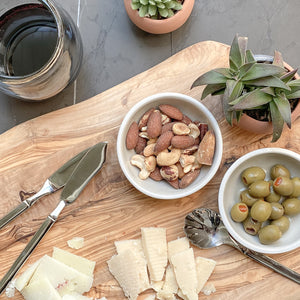 A cheese and appetizer plate featuring nuts and olive in Mexican ceramic dishes, alongside red wine, cheese and succulents.