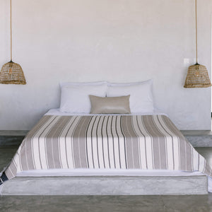 A mini leather lumbar pillow on a bed with a desert stripes cotton coverlet.