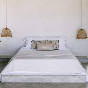 A mini leather lumbar pillow stacked against a larger lumbar pillow on a white beachy bed.