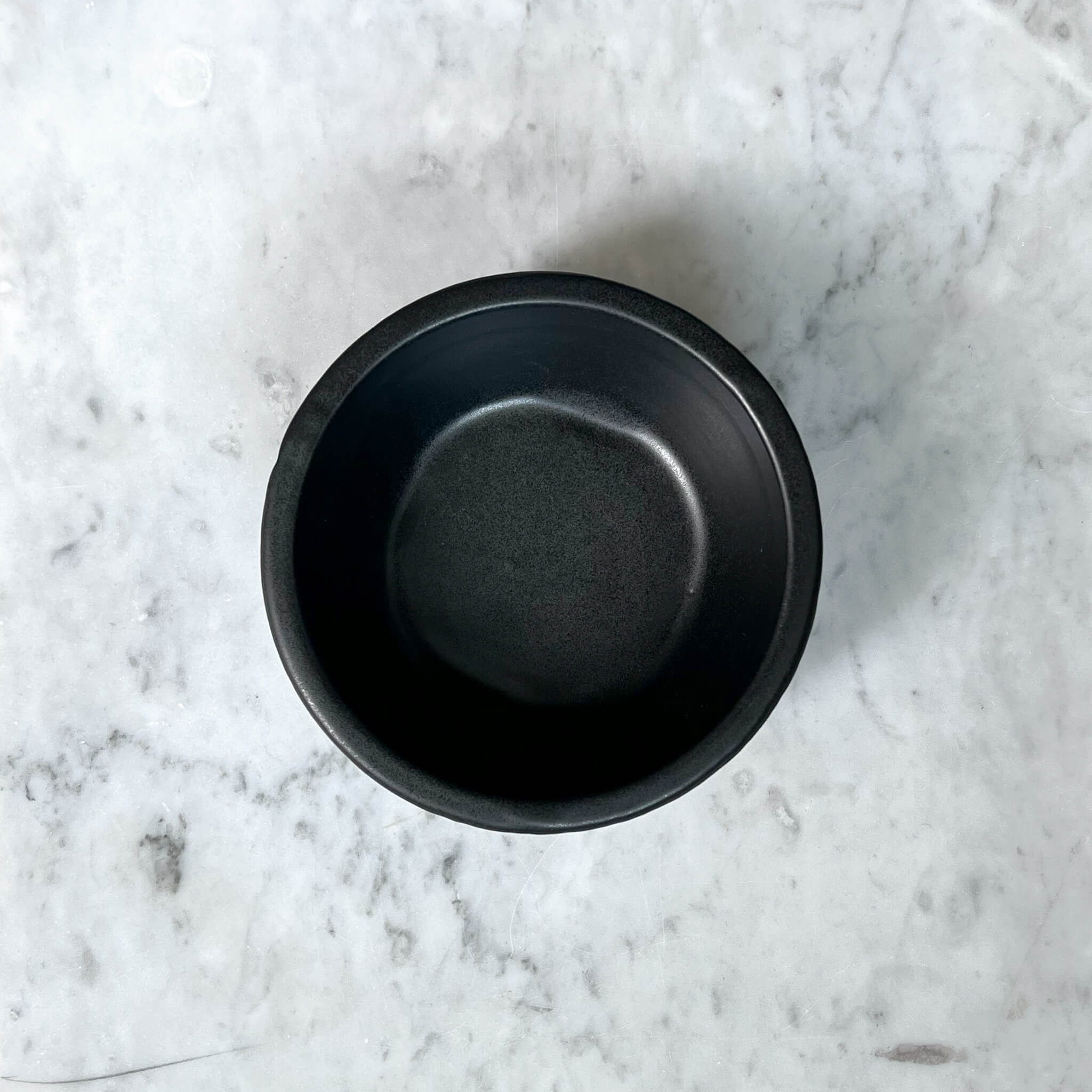 A ceramic molcajete in black on a marble counter.