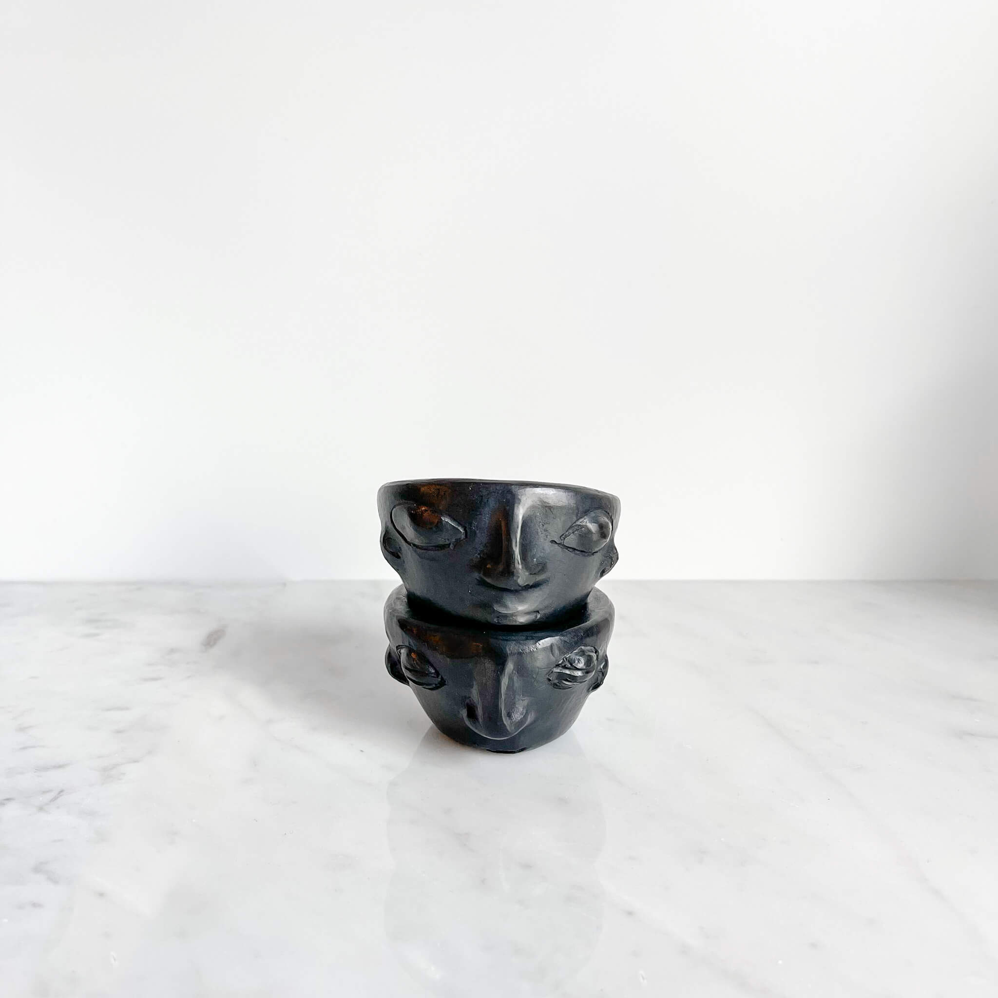 A pair of Oaxaca black clay copitas with faces on a marble counter.