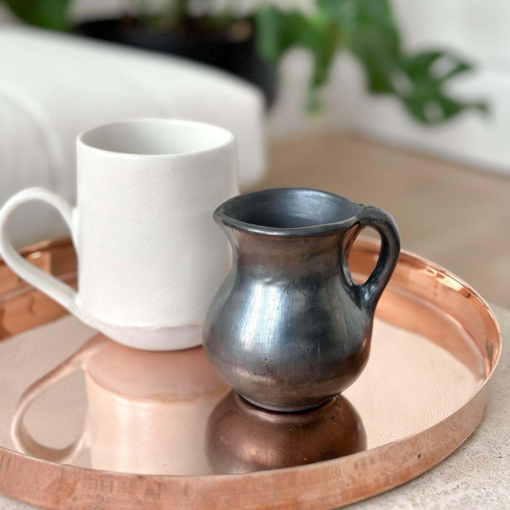 Oaxaca black clay creamer with a white mug on a copper tray.