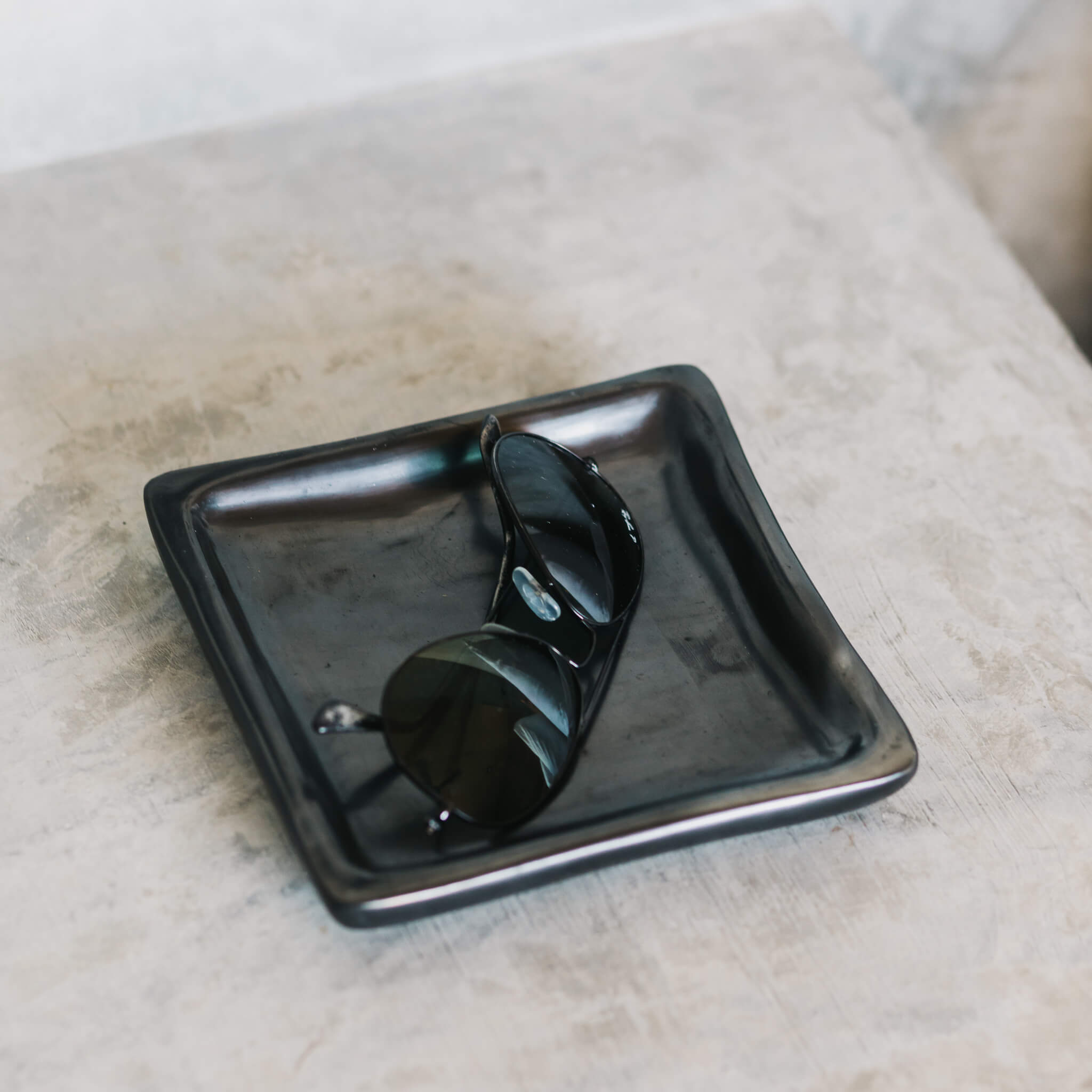 A Oaxaca pottery black clay plate used as a catchall for Raybans.