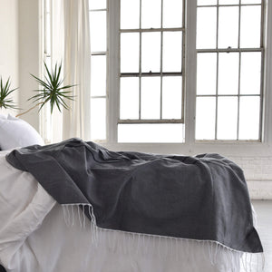 A Oaxaca cotton dark gray coverlet on a bed in a brightly lit urban loft.