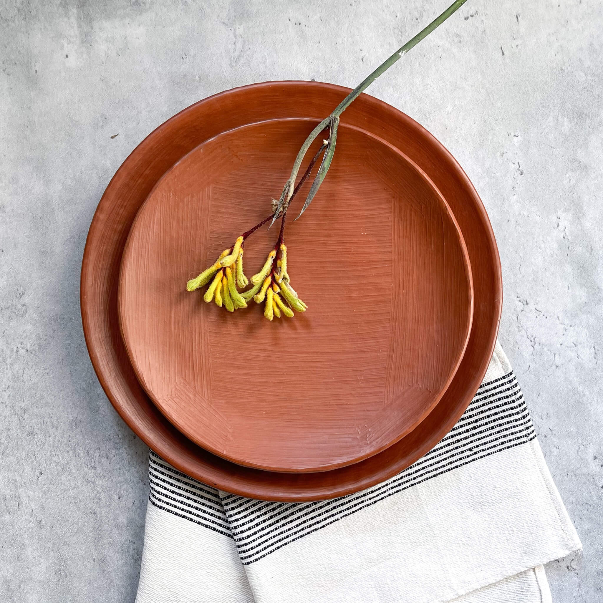A Oaxaca red clay salad plate and dinner plate set, a top a cotton towel with a floral sprig.