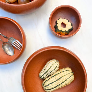 A series of Oaxaca red clay serving bowls on with various vegetable slices.