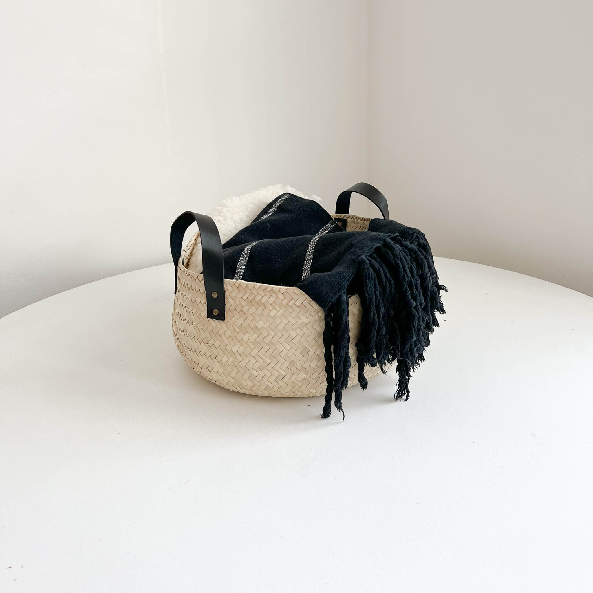 A large Oaxaca storage basket with black leather handles with a black towel and sheep shearling inside.
