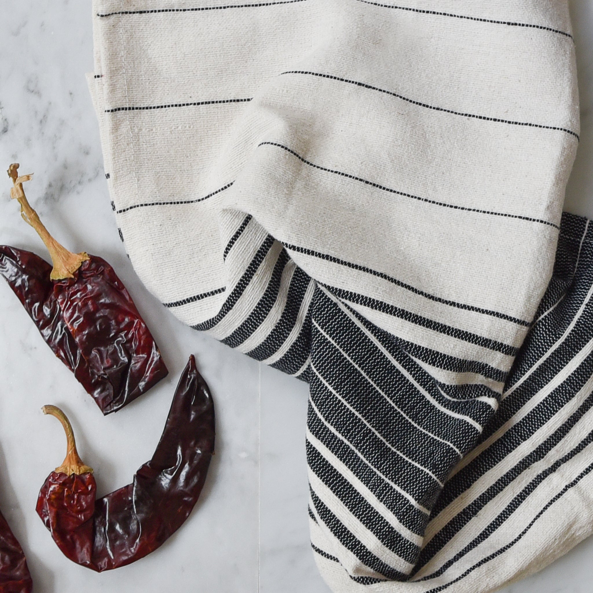 Black and ivory kitchen hand towel on a white marble counter with dried red peppers.