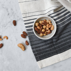 An ivory, black and grey hand towel on a white marble counter with a bowl of mixed nuts.
