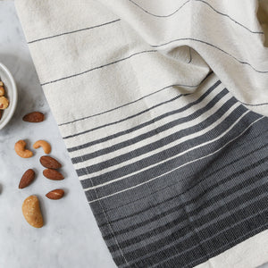 A handwoven Oaxacan hand towel on a white marble counter next to a bowl of nuts.