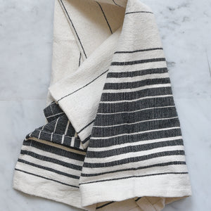 An ivory and black striped hand towel handwoven in Oaxaca, Mexico on a marble counter.