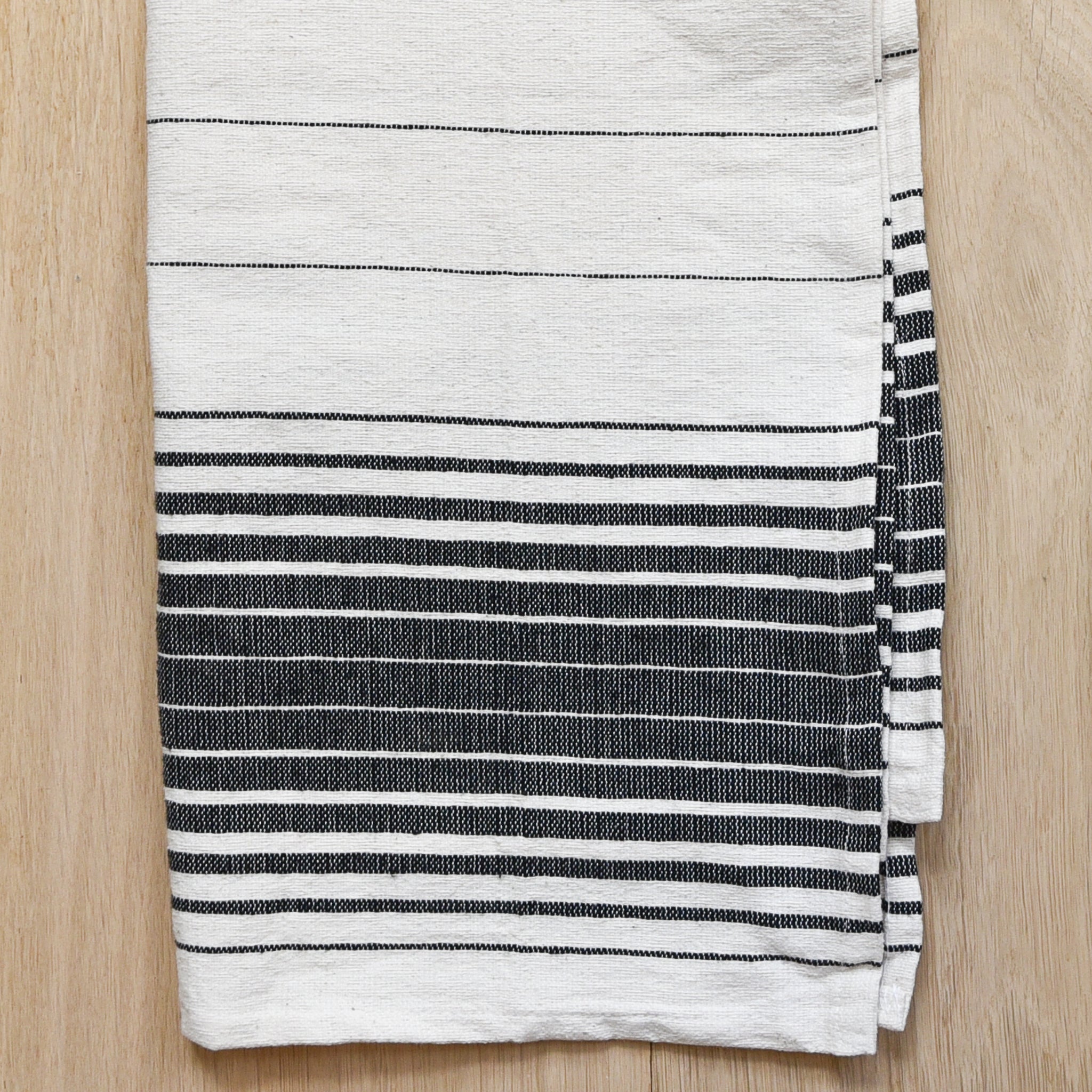 A black and ivory kitchen towel on a light wood table.