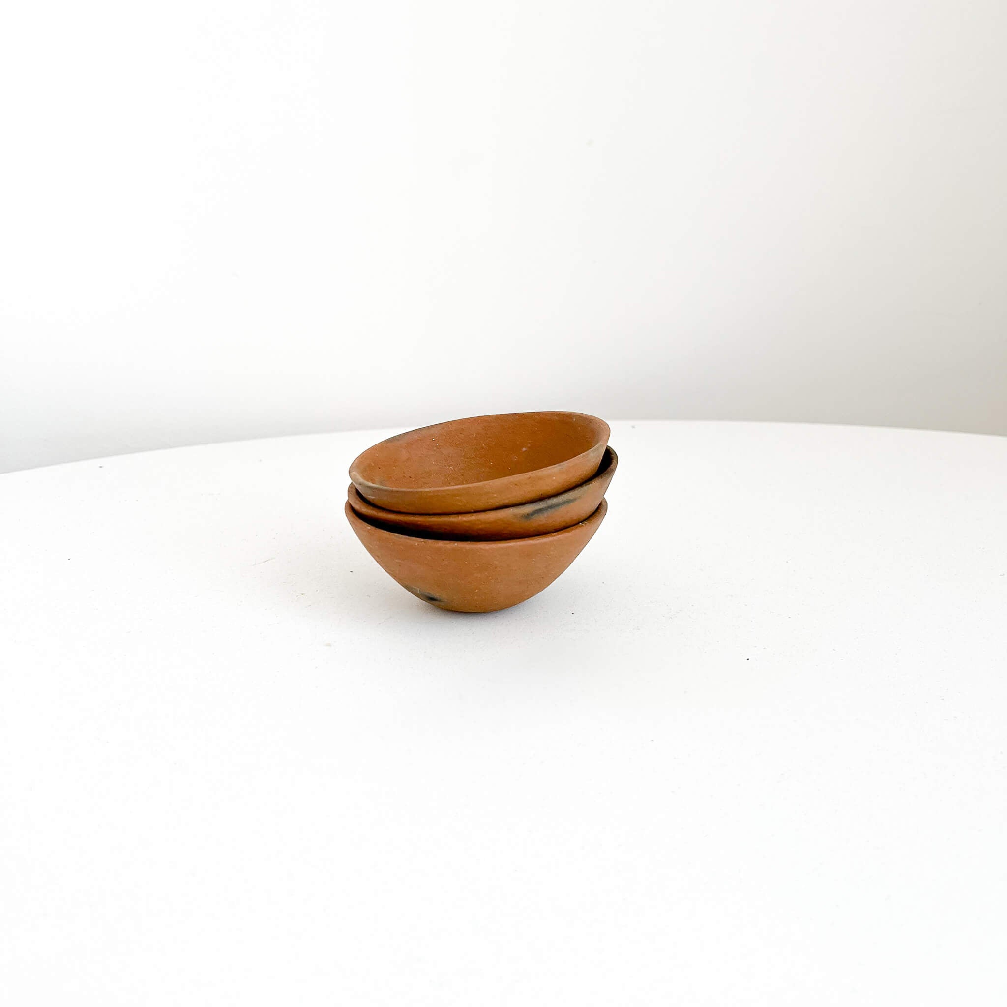 A set of small clay Pai Pai bowls on a white table.