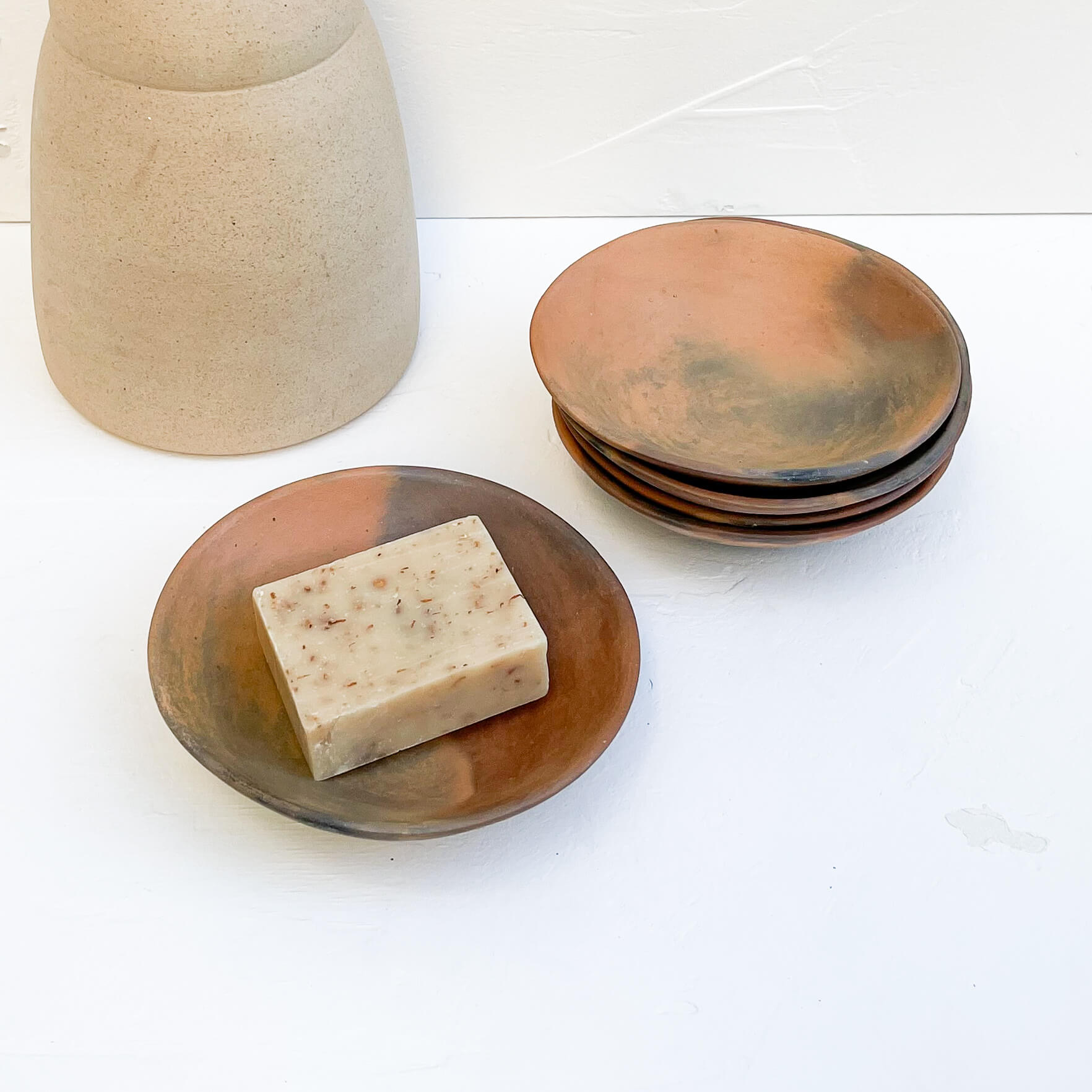 A collection of small clay plates made by the Pai Pai community with a bar of soap and ceramic vase.
