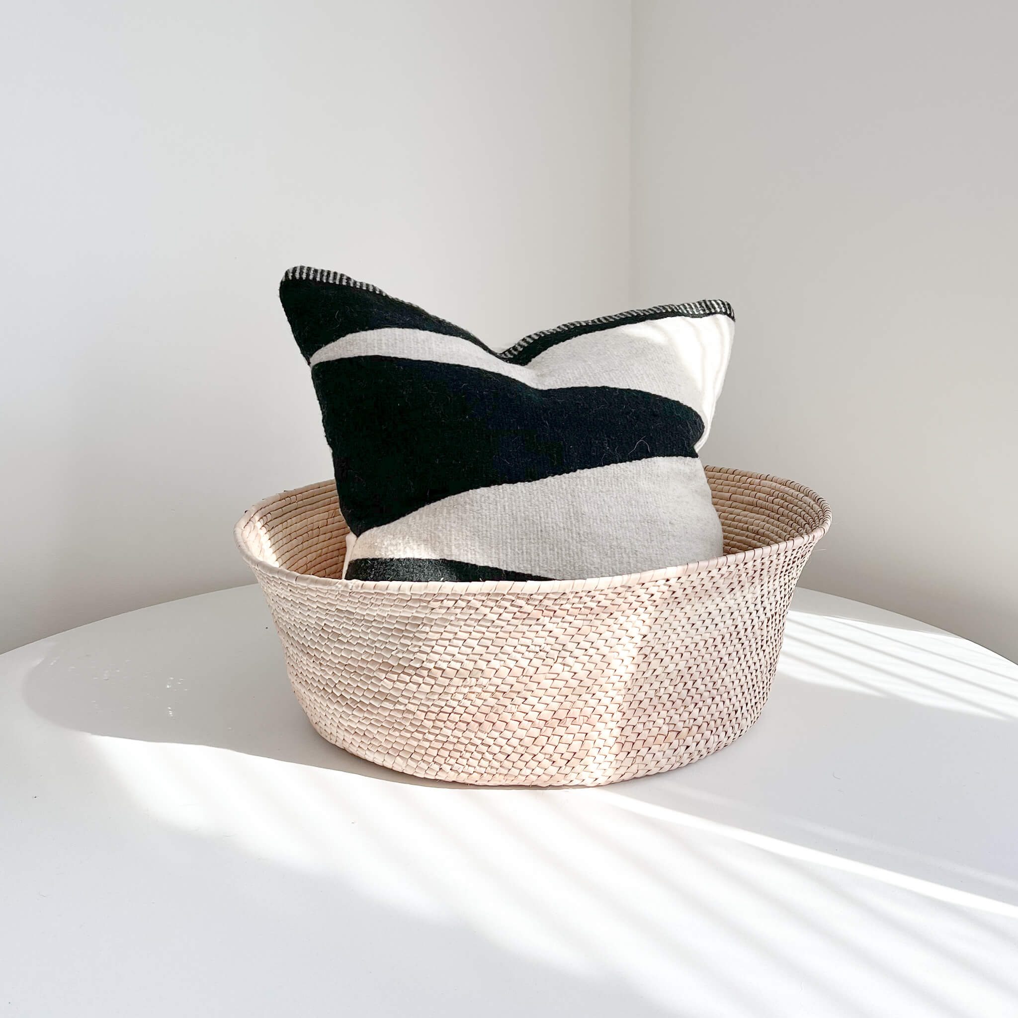 Large palm floor basket on a white table holding a large pillow.