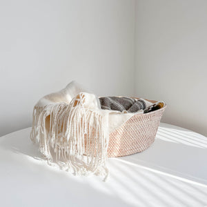 A large palm storage floor basket with a blanket on a white table.