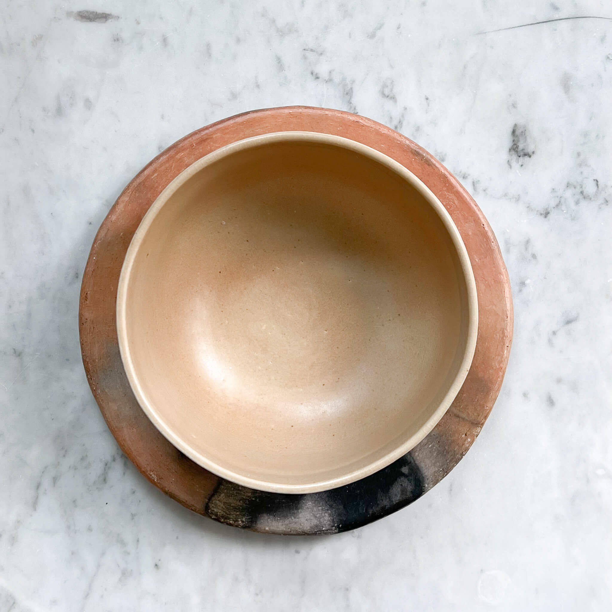 A sand colored serving bowl stacked on a smoked orange clay plate.
